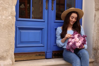 Photo of Beautiful woman with bouquet of spring flowers near building outdoors, space for text