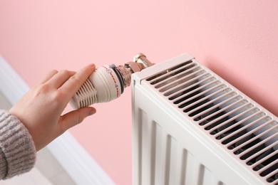 Photo of Woman adjusting heating radiator near color wall