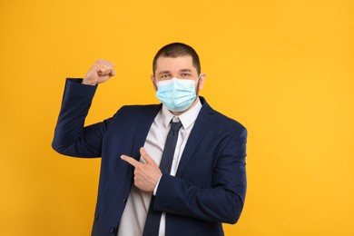 Photo of Businessman with protective mask showing muscles on yellow background. Strong immunity concept