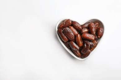 Photo of Heart shaped bowl with sweet dried date fruits isolated on white, top view. Space for text