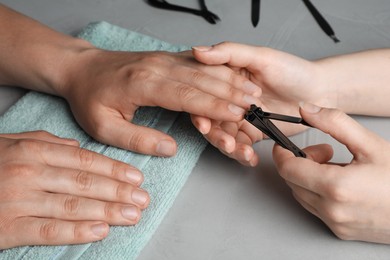 Photo of Professional manicurist working with client at grey table, closeup