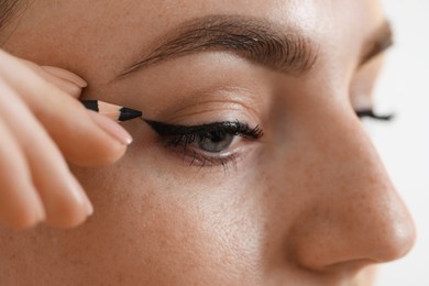 Photo of Makeup product. Woman applying black eyeliner on blurred background, closeup