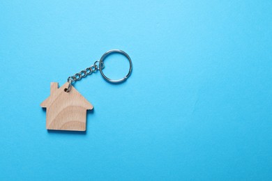 Photo of Wooden keychain in shape of house on light blue background, top view. Space for text