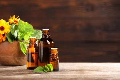 Photo of Bottles with essential oils, mint and flowers on wooden table. Space for text