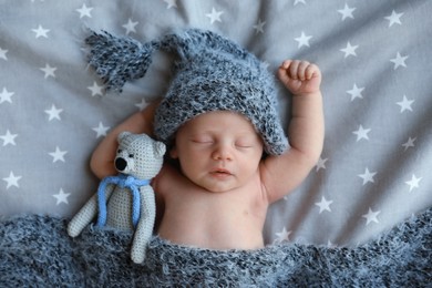 Photo of Cute newborn baby in warm hat with toy sleeping on bed, top view