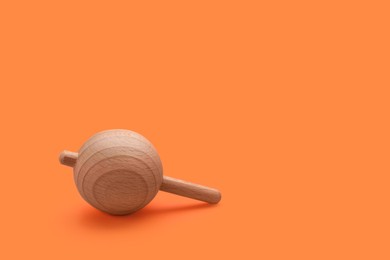 Photo of One wooden spinning top on orange background, space for text. Toy whirligig