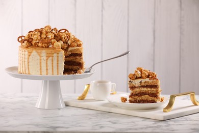 Photo of Caramel drip cake decorated with popcorn and pretzels served on white marble table