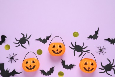 Photo of Flat lay composition with paper bats, plastic pumpkin baskets and spiders on light violet background, space for text. Halloween decor