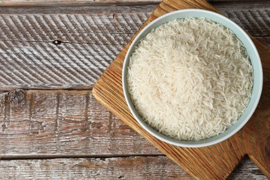Photo of Raw basmati rice in bowl on wooden table, top view. Space for text