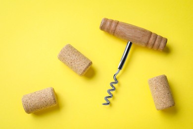 Photo of Corkscrew and wine bottle stoppers on yellow background, flat lay