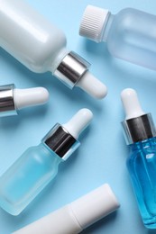Photo of Many bottles and tube of cosmetic serum on light blue background, flat lay