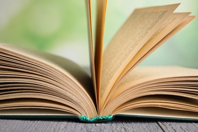 Photo of Open book on grey wooden table against blurred green background, closeup