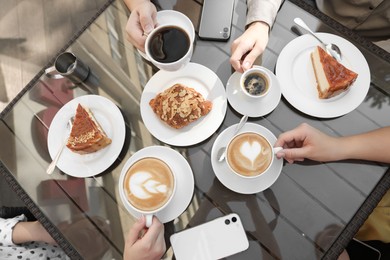 Photo of Friends drinking coffee at wooden table in outdoor cafe, top view