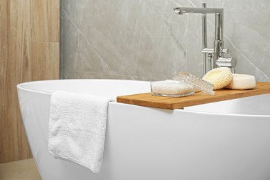 Photo of Soft bath towel and personal care products on tub tray in bathroom