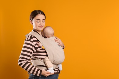 Photo of Mother holding her child in sling (baby carrier) on orange background. Space for text