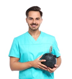 Photo of Portrait of young male doctor holding piggy bank with money on white background