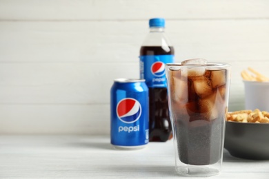 Photo of MYKOLAIV, UKRAINE - FEBRUARY 15, 2021: Glass of Pepsi and snack on white wooden table, space for text