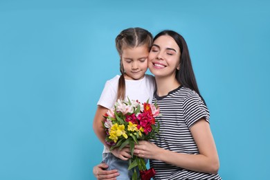 Photo of Happy woman with her daughter and bouquet of beautiful flowers on light blue background, space for text. Mother's day celebration