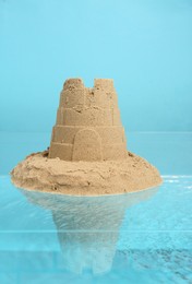 Photo of Pile of sand with tower on rippled water against light blue background. Beautiful castle