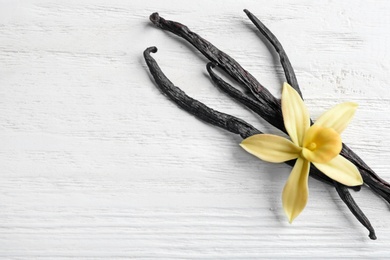 Photo of Flat lay composition with vanilla sticks and flower on wooden background. Space for text