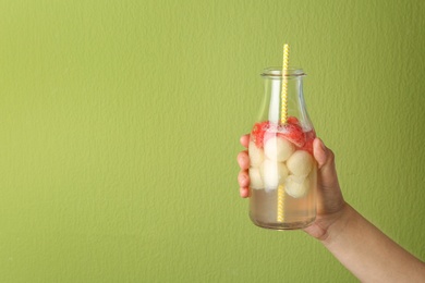 Photo of Woman holding glass bottle of melon and watermelon ball cocktail against light green background. Space for text