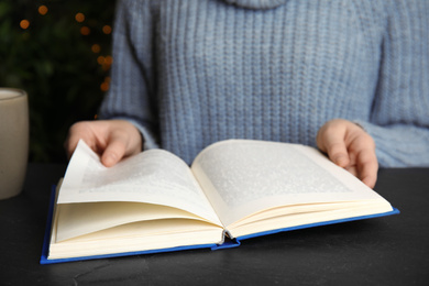 Photo of Young woman reading book at table, closeup