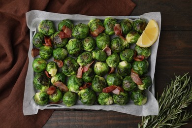 Photo of Delicious roasted Brussels sprouts, bacon, lemon and rosemary on wooden table, top view