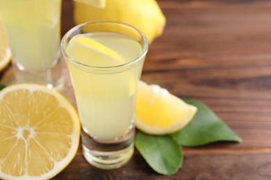 Photo of Tasty limoncello liqueur, lemons and green leaves on wooden table, closeup. Space for text