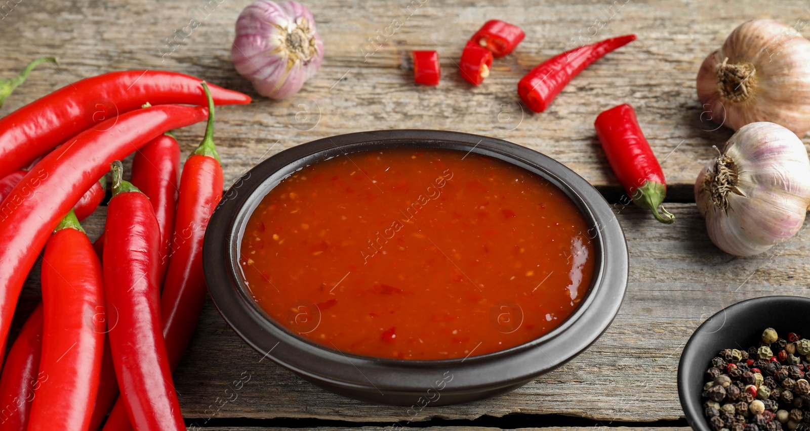 Photo of Spicy chili sauce in bowl and ingredients on wooden table, closeup