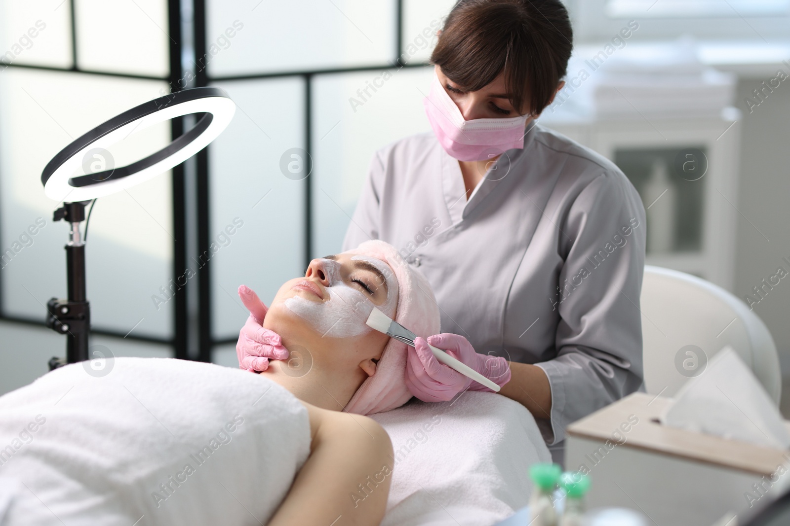 Photo of Cosmetologist applying mask on woman's face in clinic