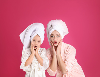 Photo of Emotional mother and little daughter in bathrobes on pink background. Space for text