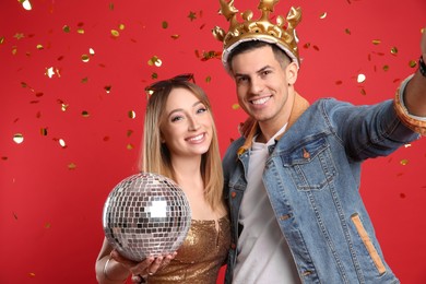 Photo of Happy couple with disco ball and confetti on red background