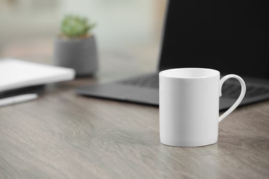 Photo of White ceramic mug and laptop on wooden table indoors. Space for text