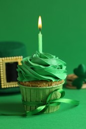 Photo of St. Patrick's day party. Tasty cupcake with burning candle and leprechaun hat on green background, closeup