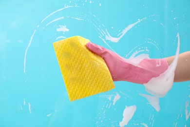 Photo of Woman cleaning glass with rag against color background
