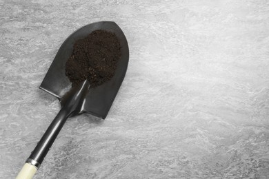 Photo of Metal shovel with fertile soil on grey textured surface, top view. Space for text