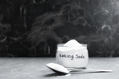 Photo of Spoon and jar with baking soda on grey table. Space for text