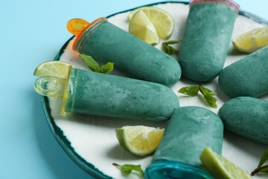 Photo of Plate with delicious spirulina popsicles, mint and lime slices on color background, closeup