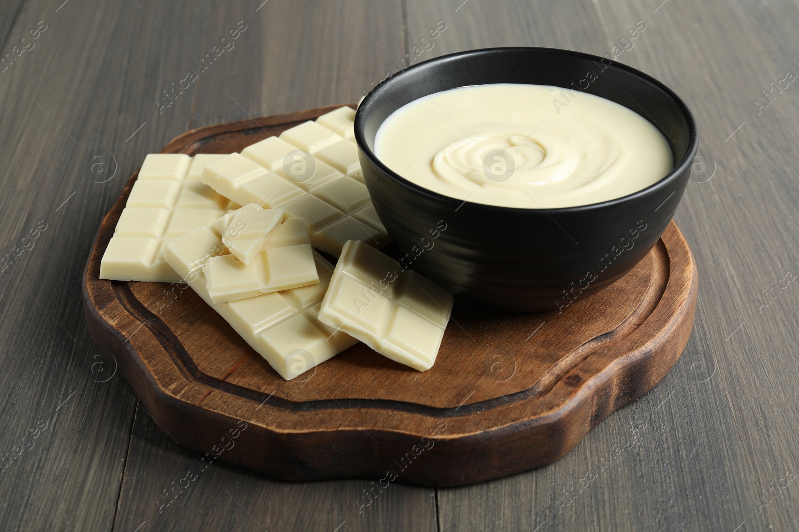 Tasty white chocolate paste in bowl and pieces on wooden table Photo of Tasty white chocolate paste in bowl and pieces on wooden table