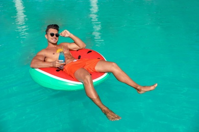 Photo of Young man with cocktail and inflatable ring in pool on sunny day