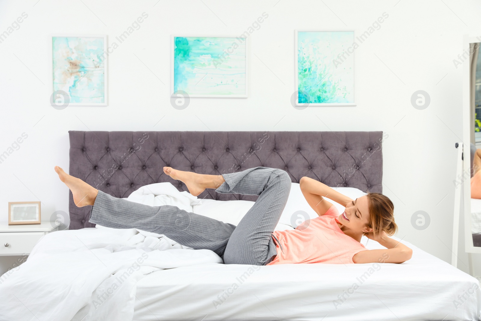 Photo of Young beautiful woman doing exercise on bed at home. Morning fitness