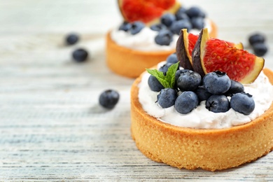 Photo of Tarts with blueberries and figs on white wooden table, space for text. Delicious pastries