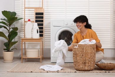 Photo of Happy woman with laundry near washing machine indoors