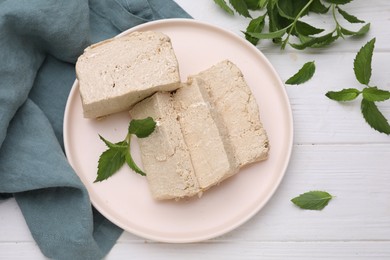 Photo of Plate with pieces of tasty halva and mint on white wooden table, flat lay