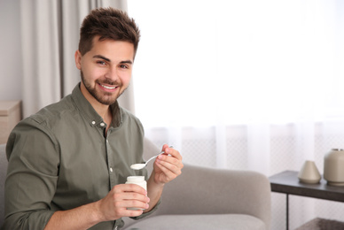 Photo of Happy young man with tasty yogurt in living room. Space for text