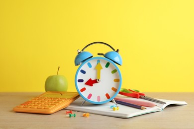 Photo of Light blue alarm clock and different stationery on white wooden table against yellow background. School time