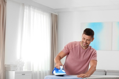 Handsome man ironing clean laundry at home, space for text