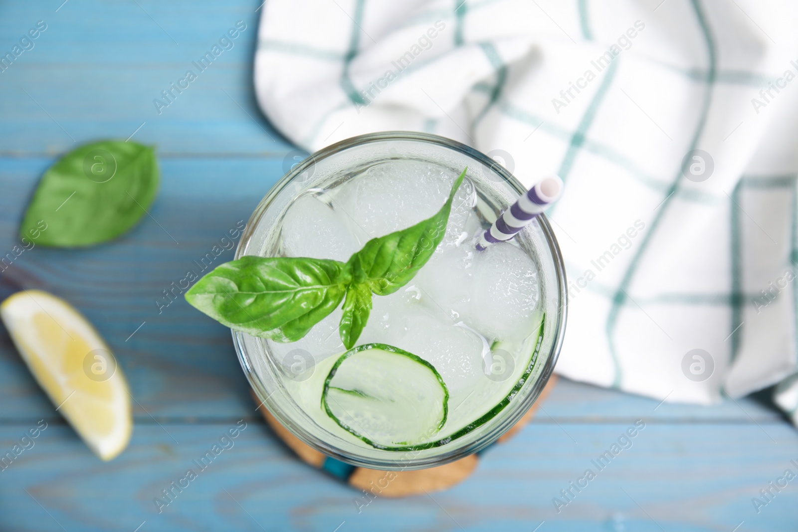 Photo of Glass of refreshing cucumber water with basil on light blue wooden table, flat lay