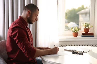 Photo of Man writing letter at white table in room