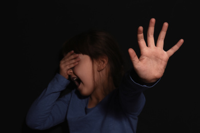 Photo of Crying little girl making stop gesture near black wall, focus on hand. Domestic violence concept